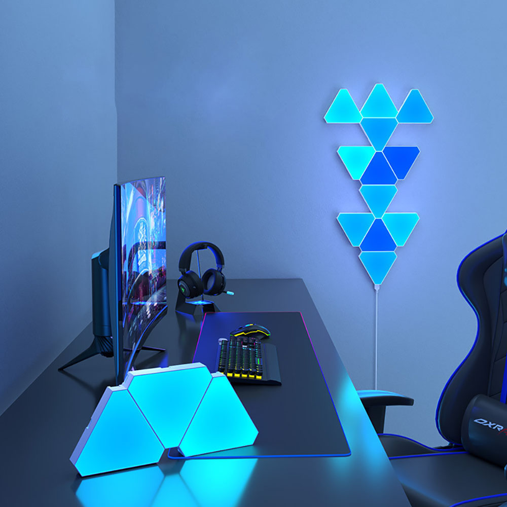 Painéis triangulares LED RGB montados na parede ao lado de uma secretária gaming.